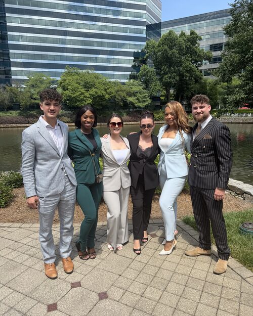 Six Winners Crest Agency team members in business attire standing together outside a corporate office